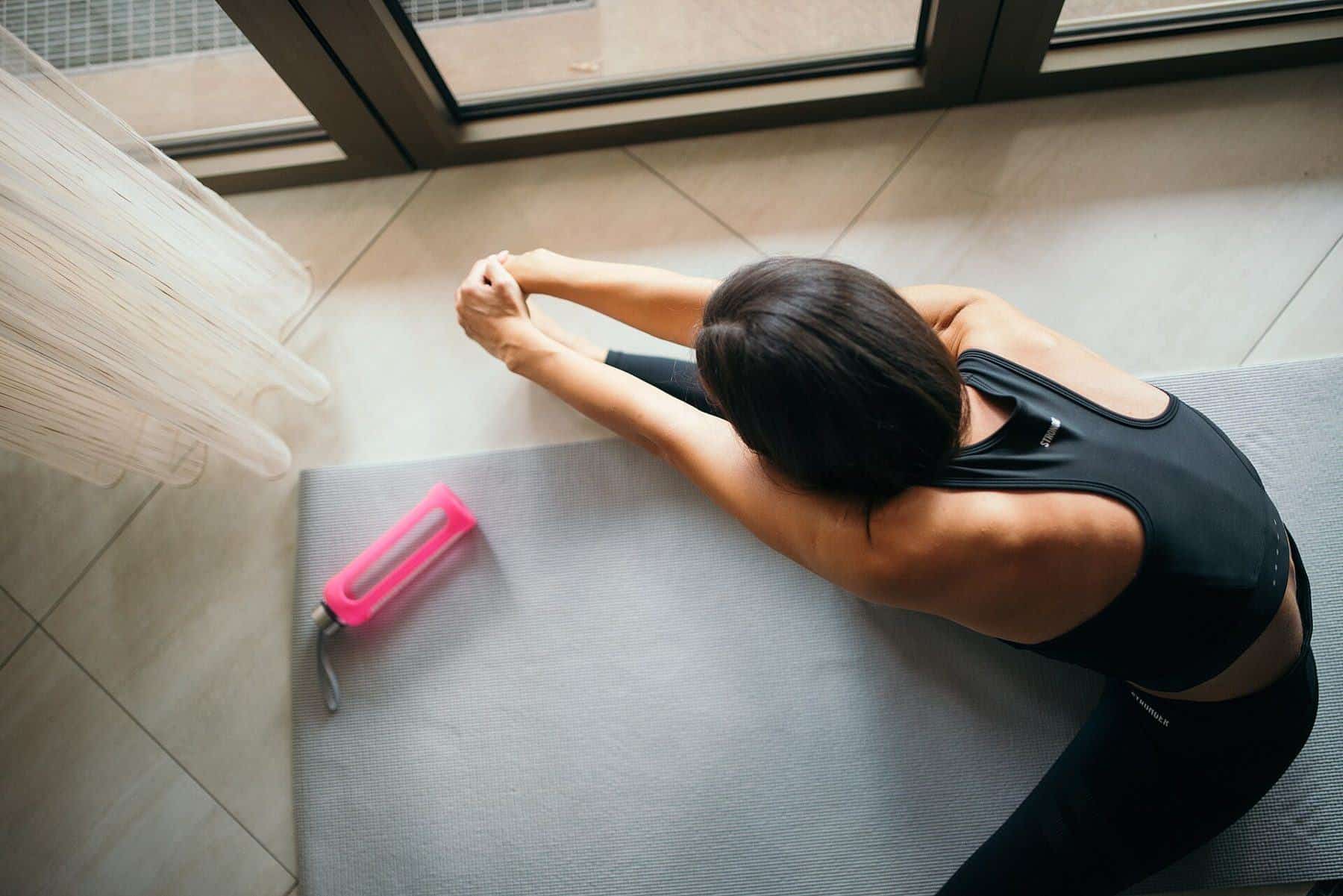 Top view of a woman seated on a mat stretching forward over her legs