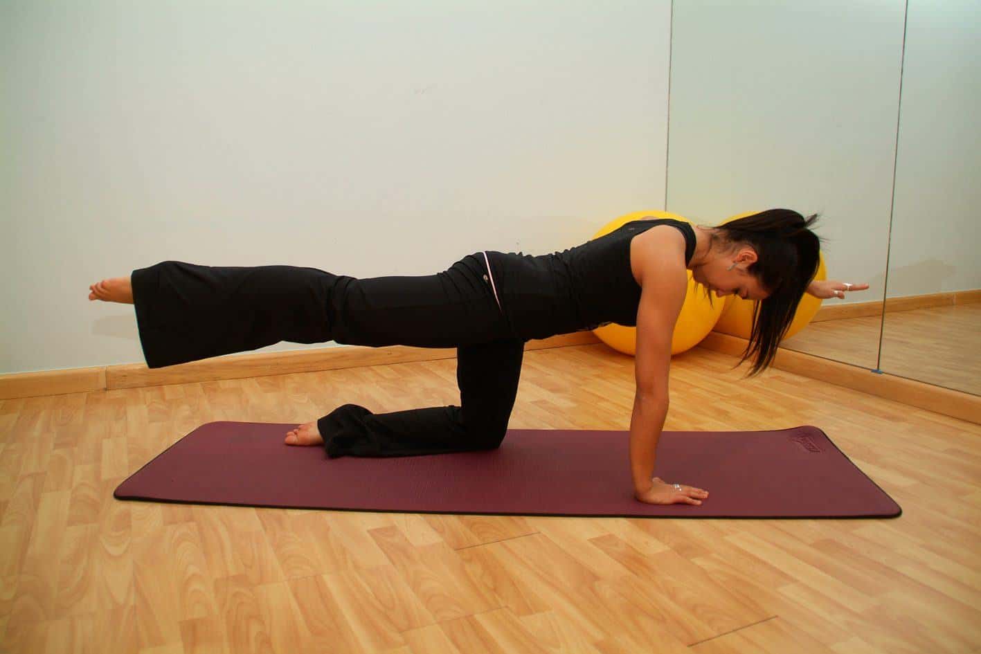 A woman on all fours on a mat extending one leg behind her in a Pilates studio