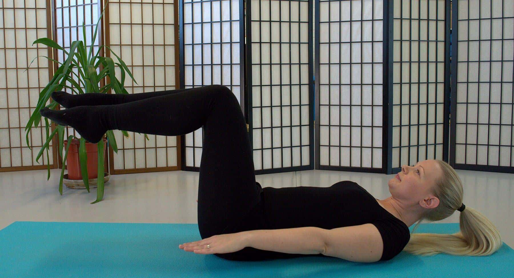 A woman lying on her back on a mat with knees bent and feet lifted
