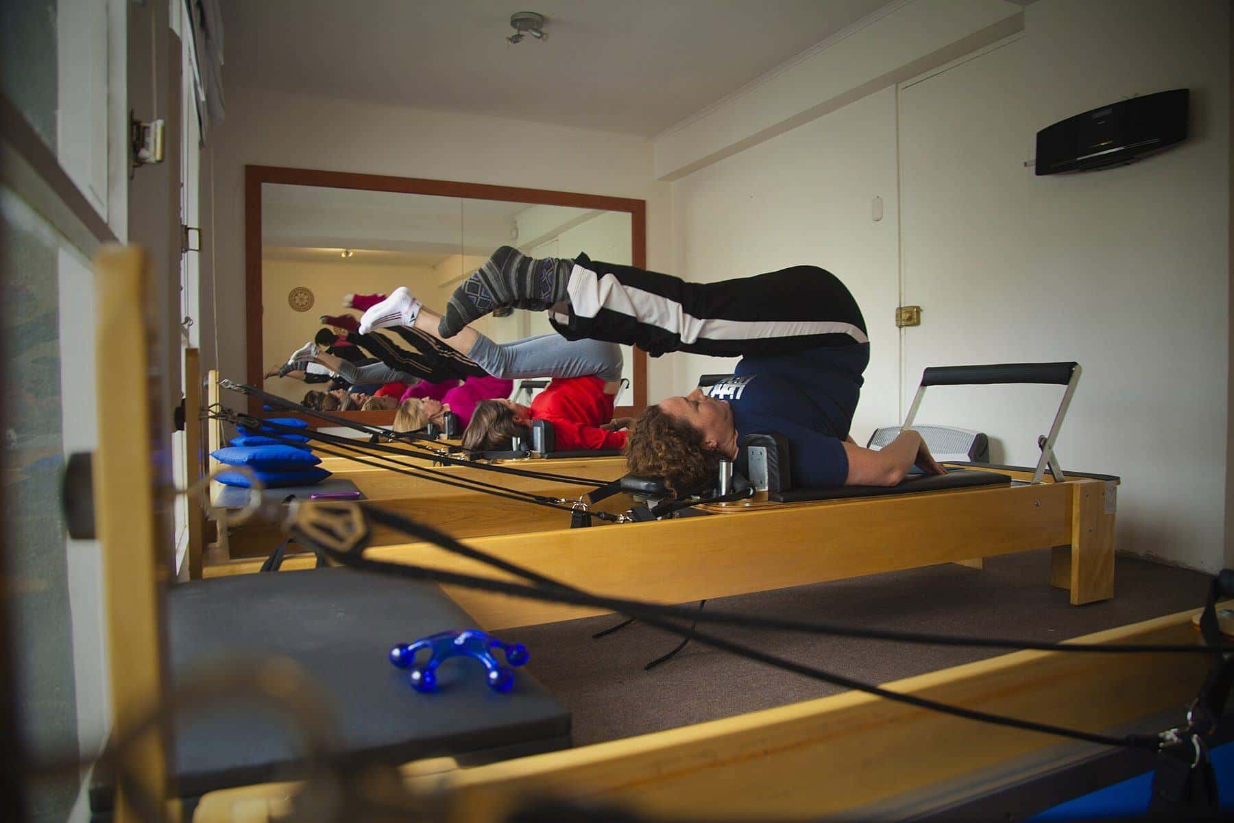A student lying on a reformer with legs raised in a studio with several reformers