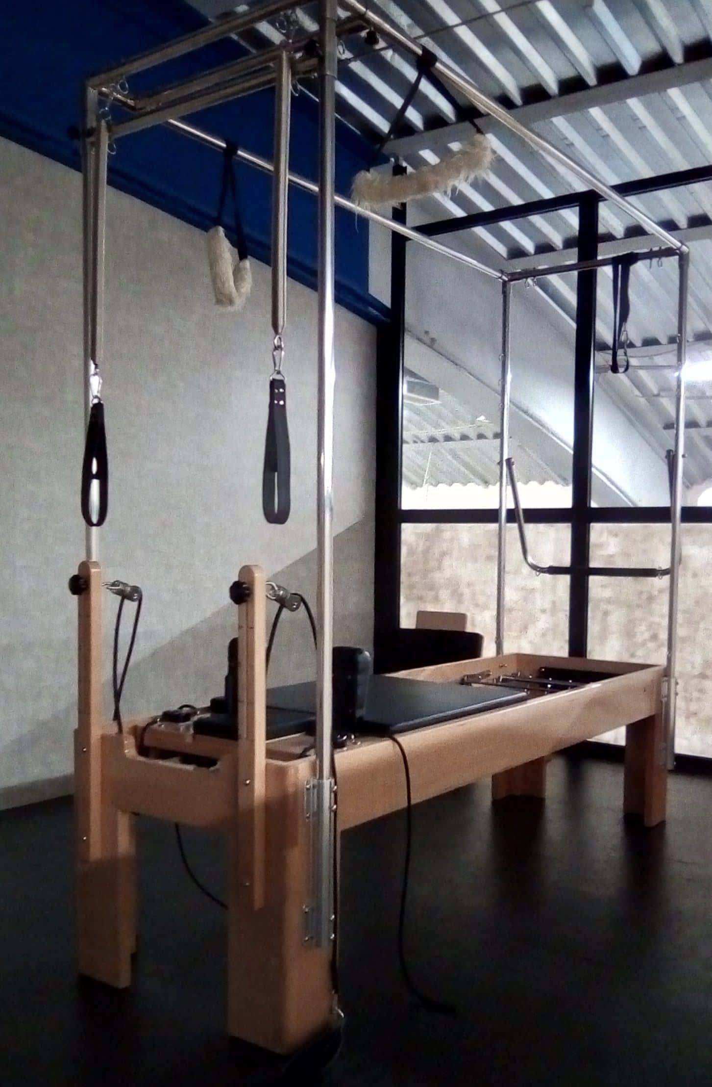 A wooden Pilates trapeze table with a metal frame, bars and springs
