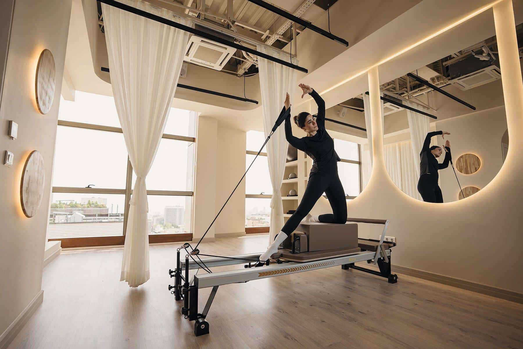 A woman using the straps on a reformer in a mirrored Pilates studio
